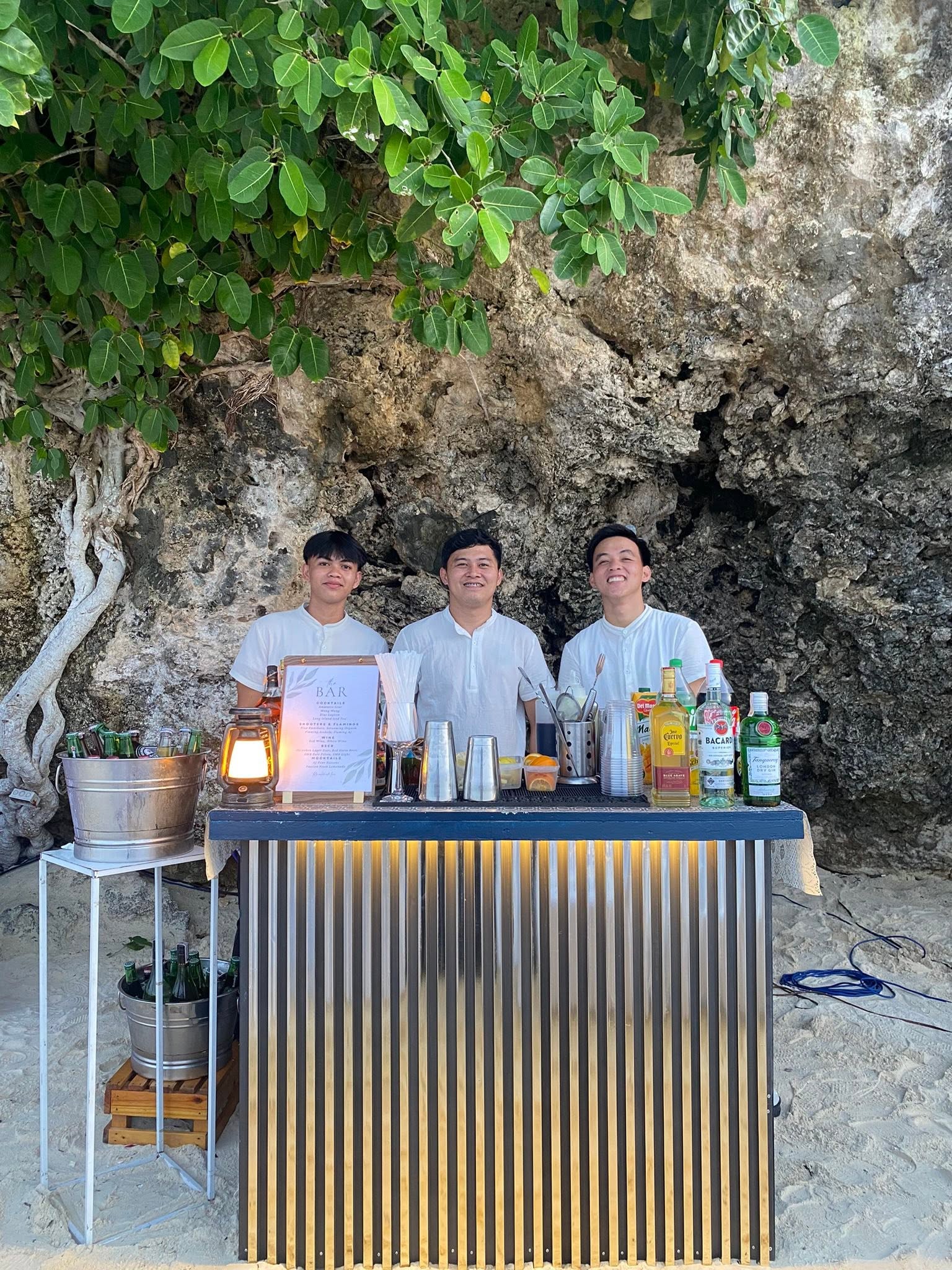 Three AJ Bohol bartenders standing behind the mobile bar at a limestone beach venue