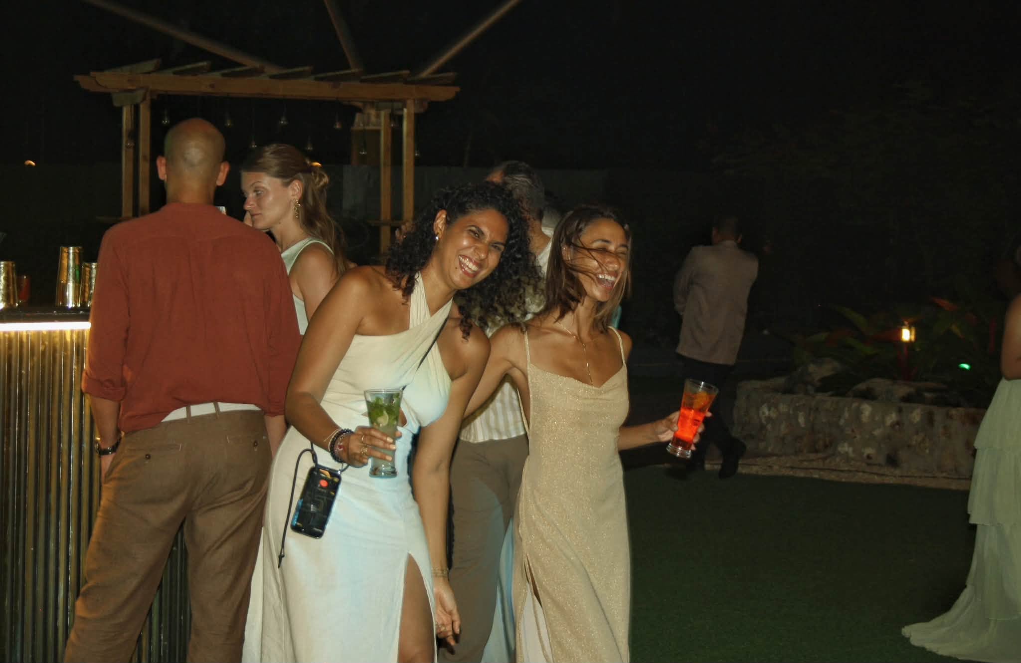Two friends laughing with cocktails at a wedding reception